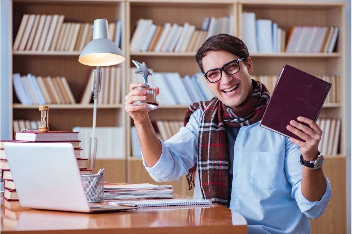 A multitasking man in a scarf, absorbed in reading a book and using a laptop